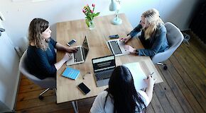 Three young women with laptops sitting on a table and working together