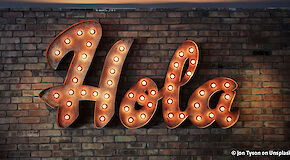The Spanish word "Hola" as illuminated lettering on a brick wall