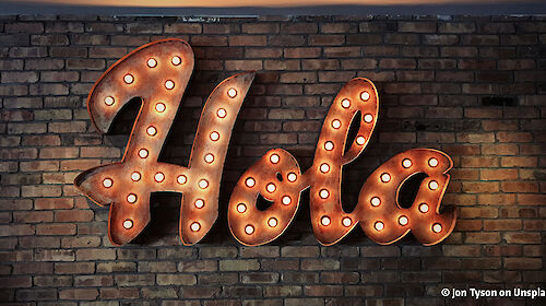 The Spanish word "Hola" as illuminated lettering on a brick wall
