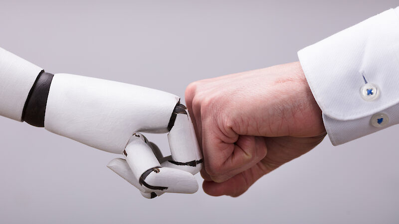 Menschliche Hand und Roboterhand machen einen "Fistbump" vor grauem Hintergrund