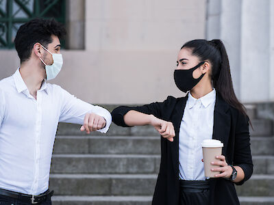 Two business people wearing face masks and bumping elbows for greeting each other outdoors