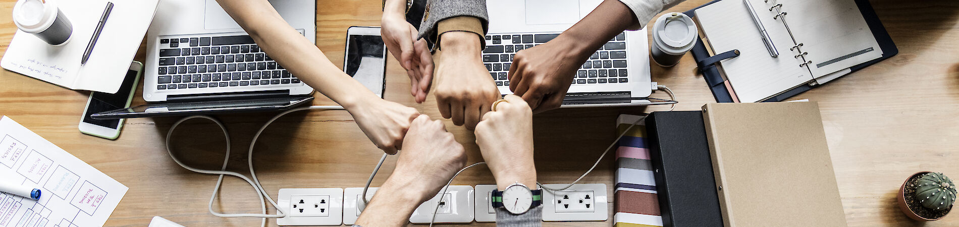 Five hands giving fistbumps in the middle of a table with laptops and stationary