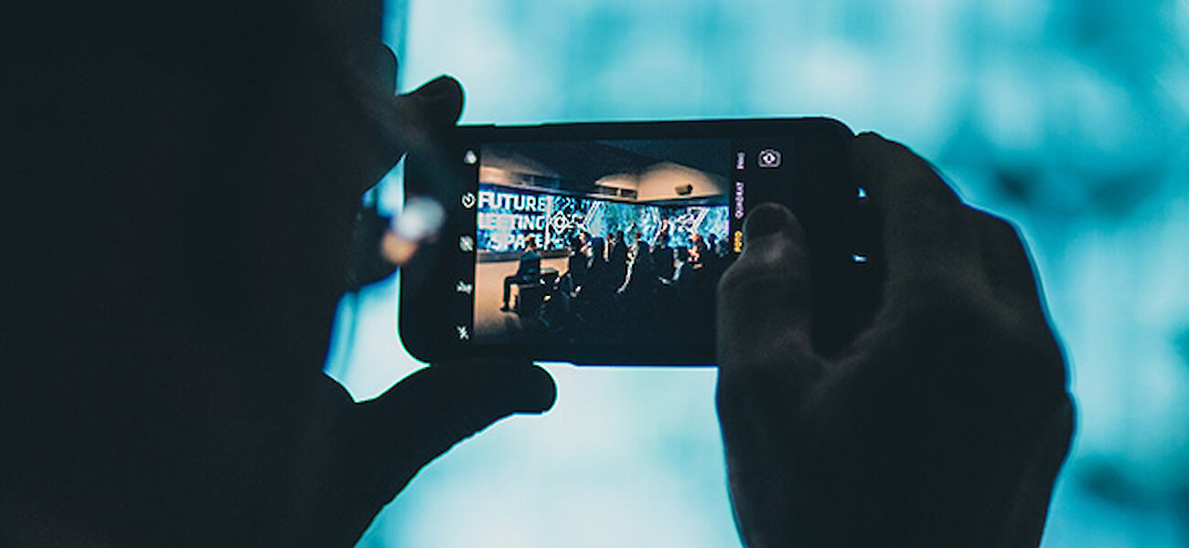 An event participant films a speaker presentation with his smartphone