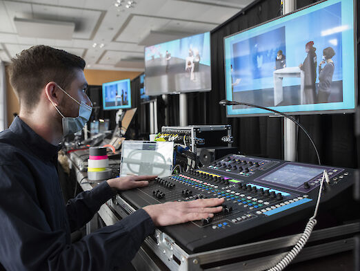 Ein Mann vor einer großen Tastatur und mehreren Monitoren im Backstage-Bereich des Streaming-Studios.
