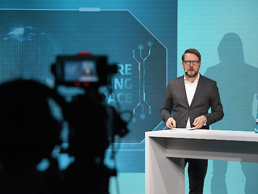 Frontal shot of Matthias Schultze at the lectern, a film camera can be seen in the foreground of the picture.