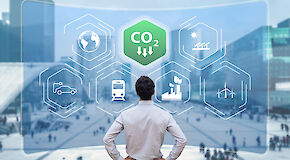 Man in business outfit stands in front of an animation on the topic "reduction of CO2 emissions