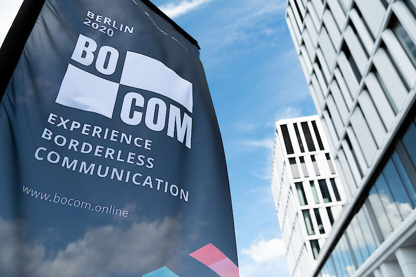 Beachflag mit Logo und Schriftzug BOCOM vor blauem Himmel und Gebäuden im Hintergrund | © GCB / Luis Bompastor