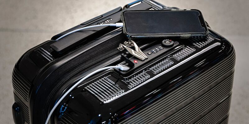 Schwarzer Hartschalen-Koffer, auf dem ein Smartphone mit angeschlossenem Ladekabel liegt.