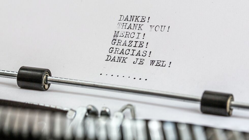 Weißes Blatt Papier in einer Schreibmaschine, auf dem Danke in sechs Sprachen getippt ist.